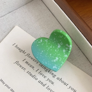 Detail of a heart-shaped hair claw clip in green gradient with white speckled texture