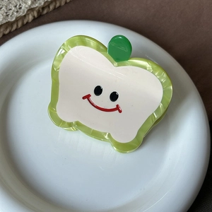 Close-up of cute green apple-shaped acetate hair claw clip with a smiling face on ceramic tray