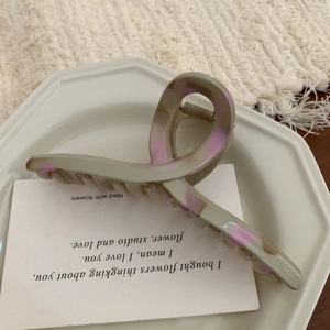 Close-up of a large grey-green hair claw clip with purple marble pattern in a ceramic tray