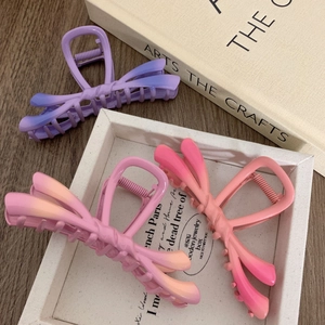 Three gradient y2k bow hair claws in matte purple, pink and yellow on wooden desk