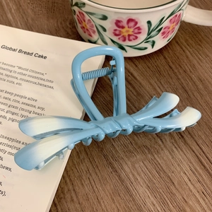 Detail view of a light blue gradient ribbon hair claw clip on an aesthetic wooden desk