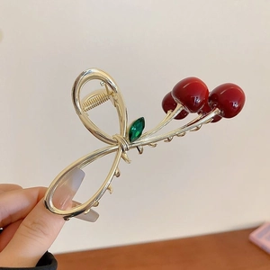 Detail of red cherry hair claw clip in polished gold metal with green gem leaf accent
