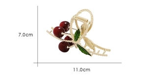 Detailed view of large gold metal hair claw clip with red cherry and green leaf accents