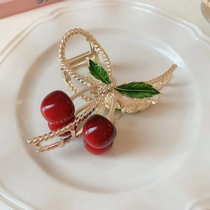 Detailed shot of golden cherry hair claw clip on white ceramic plate with red bead accents