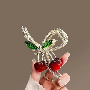 Detail of red cherry hair claw clip with golden alloy rope texture and green enamel leaves