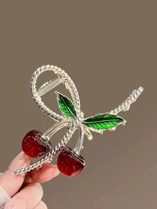 Detail of a large gold metal hair claw with translucent red cherry and green leaf accents
