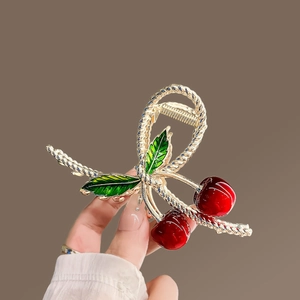 Detail of a golden metal hair claw clip with red cherry design and green leaves