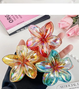 Close-up of colorful gradient plumeria hair claws in orange, yellow, and blue acrylic