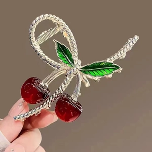 Elegant gold metal cherry hair claw clip with red fruit and green leaves held by hand
