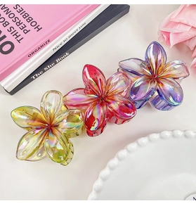 Detailed view of three iridescent flower hair claws in gradient yellow, pink, and blue shades