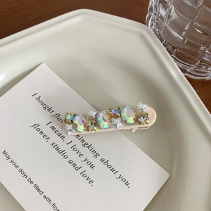 Detail of elegant hair clip with iridescent rhinestones and white stars on a white tray