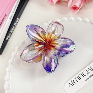 Detailed close-up of a holographic frangipani hair claw clip on a decorative white plate