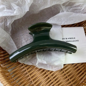 Close-up of a large dark green glossy hair claw clip with smooth curved resin teeth