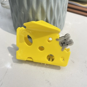 Detail shot of a yellow cheese shaped acetate hair claw clip with a cute gray mouse motif