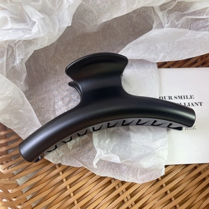 Detail of a large matte black hair claw clip with a sleek curved design on white paper