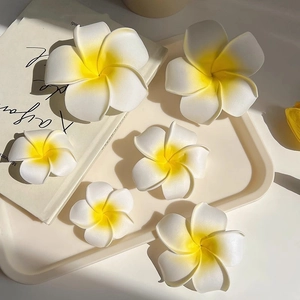Gros plan de pinces à cheveux fleurs de frangipanier blanches et jaunes en plusieurs tailles