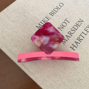 Close-up of pink acetate geometric hair clip with marble texture on linen book background