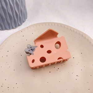 Detail view of orange cheese-shaped hair claw with a small mouse on a ceramic plate