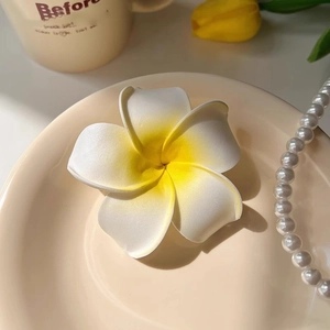 Détail d'une pince fleur de frangipanier blanche et jaune sur un plateau en céramique