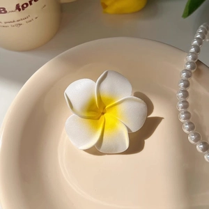 Détail d'une pince à cheveux frangipanier blanc au cœur jaune et décor de perles