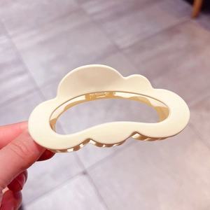 Macro detail of large matte cream cloud hair claw clip showing wavy edges and smooth texture