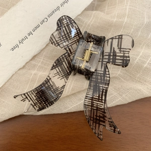 Detailed close-up of a retro black plaid bow hair claw clip with a gold metal spring