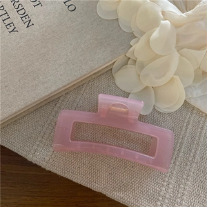 Dettaglio della grande molletta per capelli rettangolare rosa su tessuto beige con molla d'oro