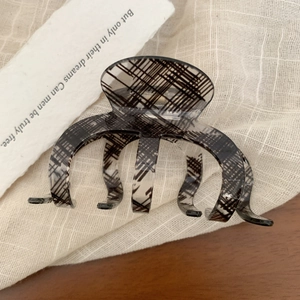 Close-up of black and white checkered acrylic hair claw clip on soft fabric texture