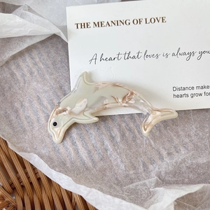 Detail showing dolphin-shaped acetate hair clip with marble pattern on a cozy background