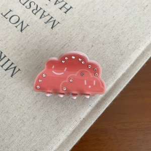 Détail de la pince à cheveux nuage en acrylique rose avec strass et motif de sourire