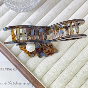 Detail view of large tortoiseshell hair claw clip with pearls on beige velvet display