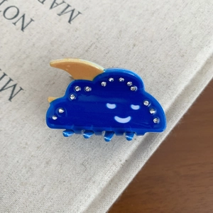 Détail d'une pince à cheveux nuage bleu avec strass et lune orange sur un livre crème