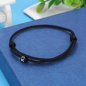 Detailed close-up of black braided cord bracelet featuring a white letter K cube bead