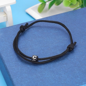 Detail of hand-woven black cord bracelet featuring a square bead with the letter C