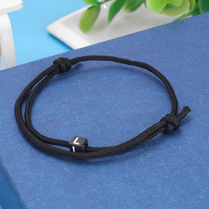 Close-up of black braided cord bracelet with adjustable knots and a letter L square bead