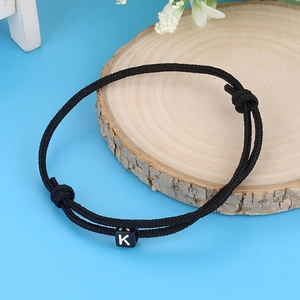 Minimalist handmade woven black cord bracelet with white letter K bead on wooden display