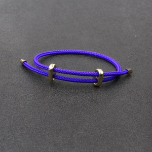 Bracelet réglable en cordon violet tressé avec boucles coulissantes dorées sur fond gris
