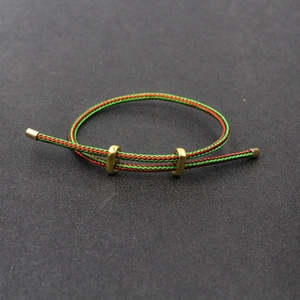 Détail du bracelet tressé rouge et vert réglable avec des éléments coulissants en laiton