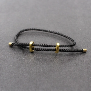 Détail du bracelet réglable en corde tressée noire avec perles coulissantes dorées