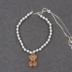 Fashionable silver beaded bracelet featuring a cute brown flocked bear pendant with bow