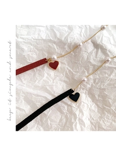 Close-up of pearl choker necklaces with red and black heart pendants on white paper