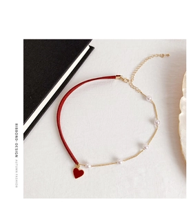 Detailed view of red ribbon choker with white pearls and heart pendant on white fabric