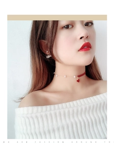 Detail of a red heart pendant choker with pearls and velvet ribbon on a female model