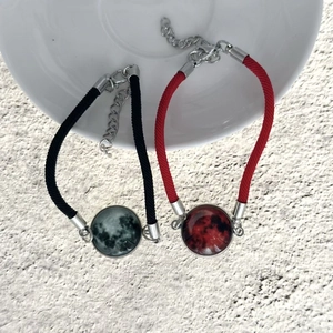 Dettaglio di bracciali intrecciati di coppia con ciondoli sole luna e chiusura a moschettone