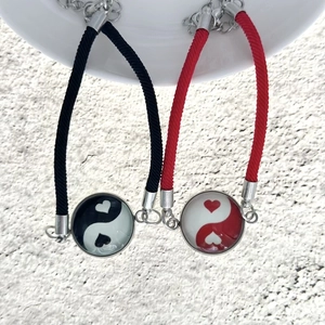 Dettaglio di bracciali di coppia intrecciati rosso e nero con ciondoli cuore yin yang su ceramica