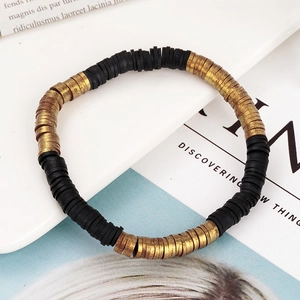 Detail van de zwarte en gouden Heishi-kralenarmband op een wit keramisch dienblad