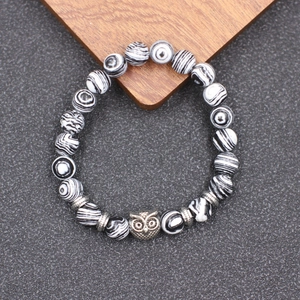 Détail du bracelet en perles rayées avec breloque chouette sur fond de bois
