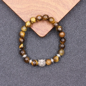 Bracelet en perles œil de tigre avec breloque hibou sur fond bois et pierre rustique