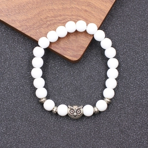 Détail du bracelet en perles blanches mates avec charm chouette sur un plateau en bois