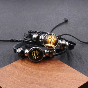 Detail of woven leather bracelets featuring luminous cross and Virgo zodiac charms